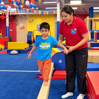 Boy walking a balance beam with a coach holding his hand at My Gym Ludhiana